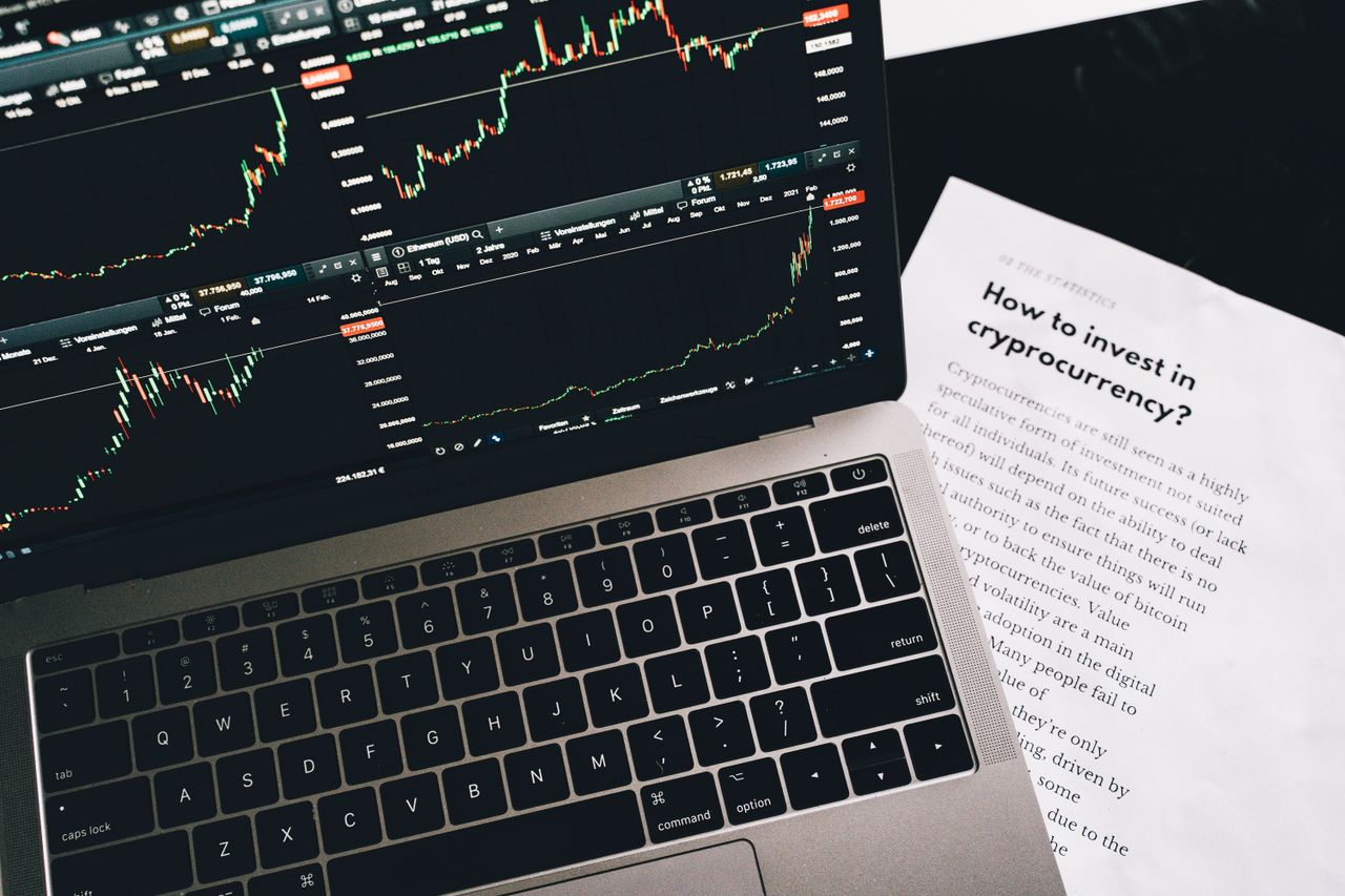 about-01 Close-up of a laptop displaying stock market graphs with a paper on investing in cryptocurrency, indoors.